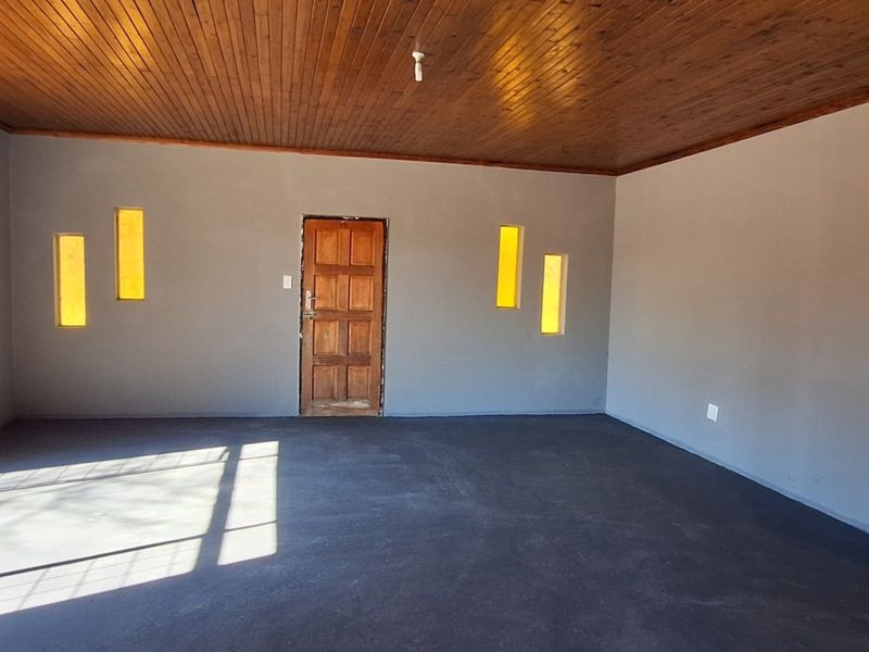 An empty living area featuring a warm timber ceiling, unique vertical inset windows, and a solid wood entrance door with dark screeded concrete flooring.