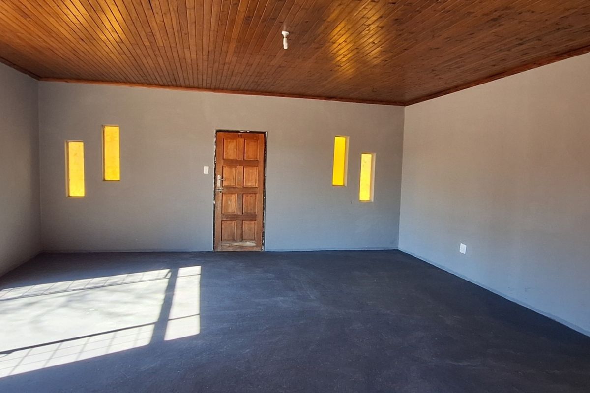 An empty living area featuring a warm timber ceiling, unique vertical inset windows, and a solid wood entrance door with dark screeded concrete flooring.