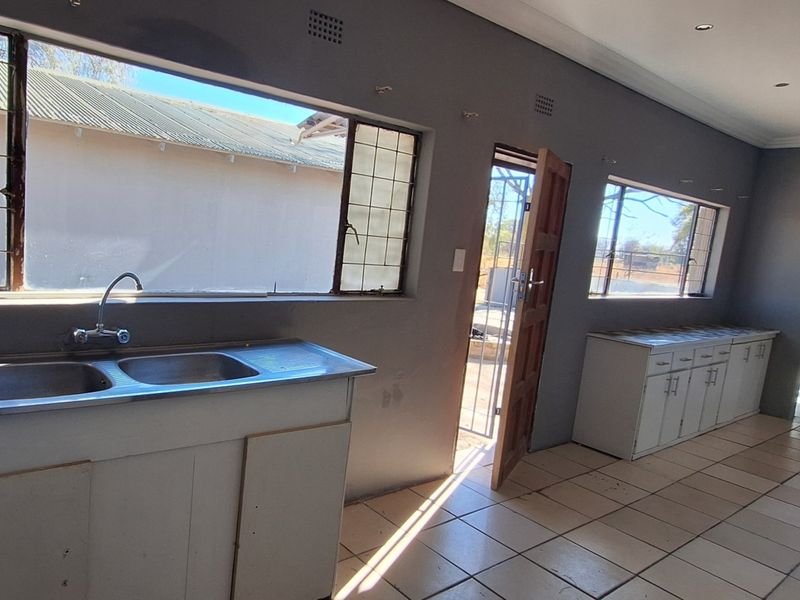 An empty kitchen area featuring tiled flooring, built-in base cabinetry with a double sink, and direct access to the exterior through a timber door.