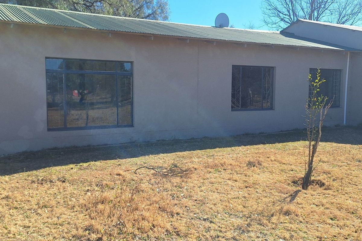 Rear view of the property featuring a corrugated metal roof, aluminium window frames with security bars, and a large garden area.