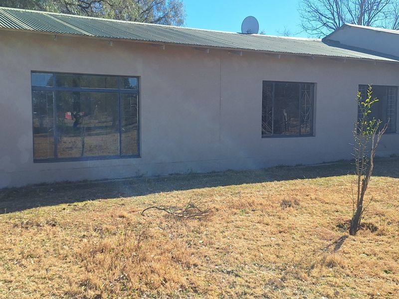 Rear view of the property featuring a corrugated metal roof, aluminium window frames with security bars, and a large garden area.