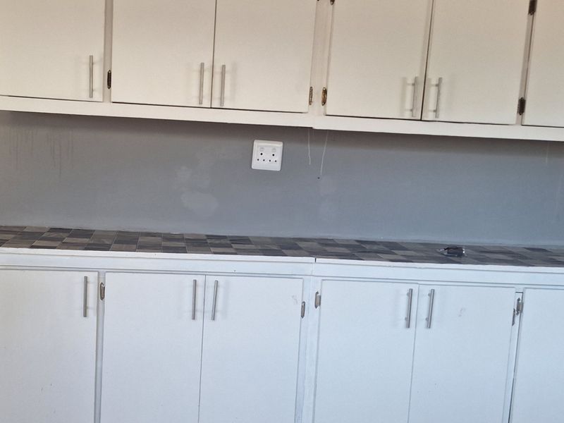A kitchen area featuring white built-in cabinetry and a tiled countertop, requiring minor cosmetic updates to the wall and cabinet finishes.