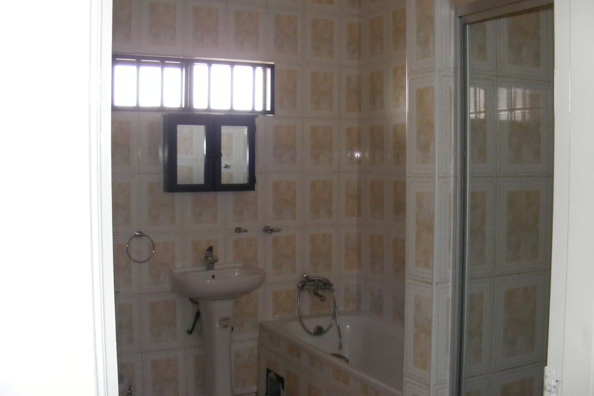 A functional bathroom featuring a pedestal basin, bathtub, and separate shower enclosure with dated wall tiling.