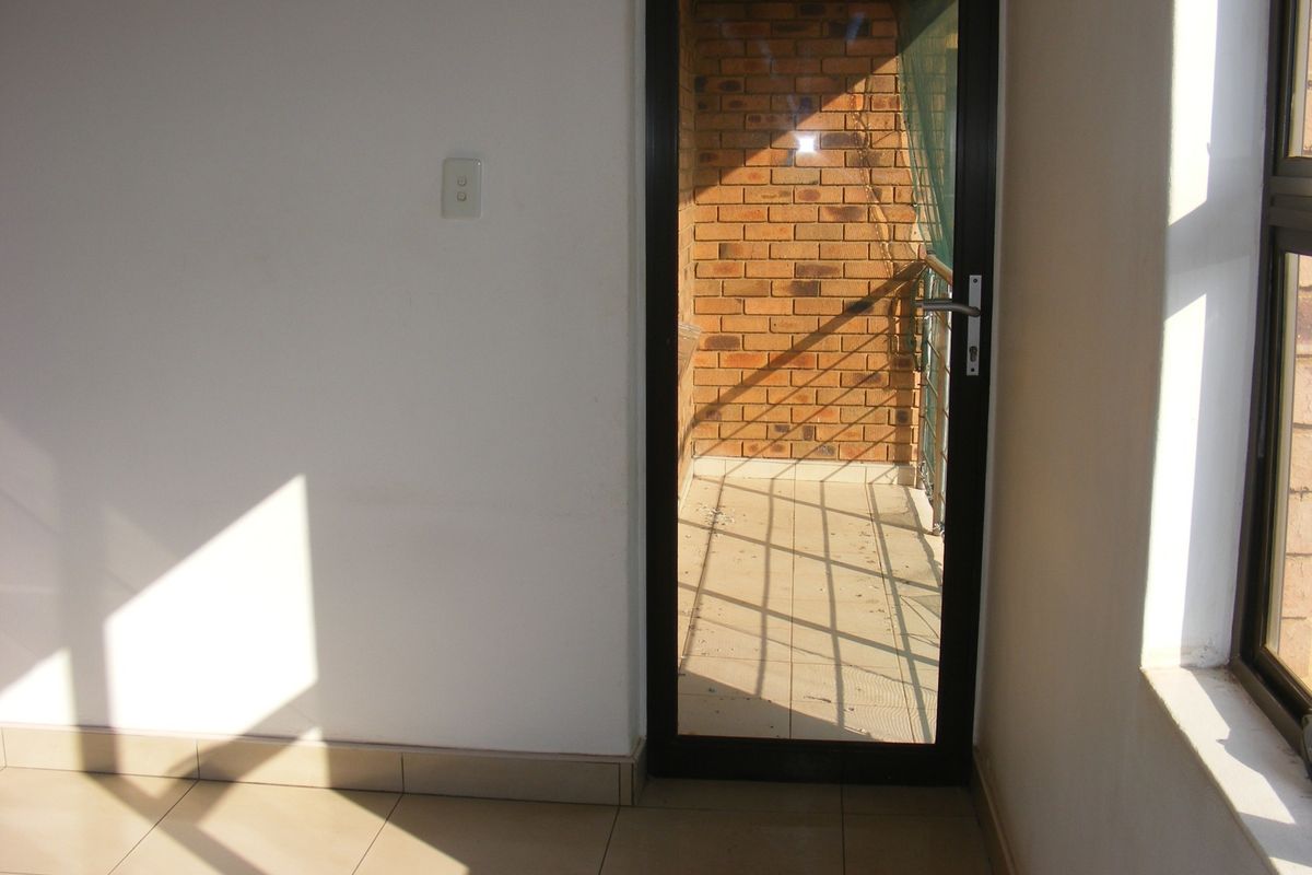 An empty living area featuring tiled flooring and a glass door leading to a brick-walled balcony, providing natural light and outdoor access.