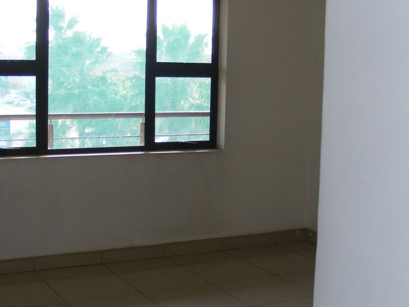 An empty bedroom featuring neutral tiled flooring and large aluminium-framed windows providing natural light.