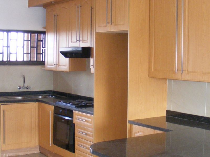 A functional kitchen featuring light wood-finish cabinetry, dark granite countertops, a built-in oven, gas hob, and a double sink with tiled backsplash.