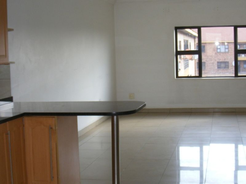 An open-plan kitchen and living area featuring tiled flooring, laminate cabinetry with granite countertops, and a breakfast bar, offering a bright, functional space.