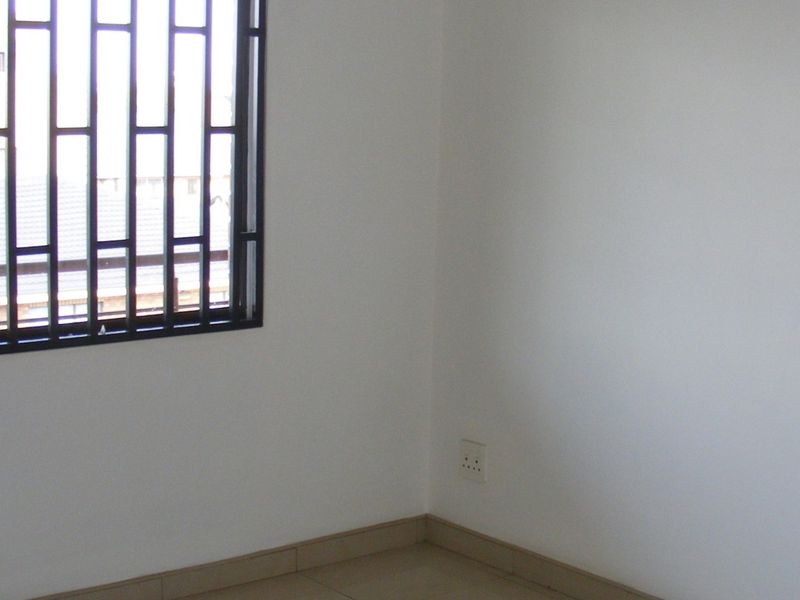 An empty bedroom featuring tiled flooring, white walls, and a window fitted with black security bars.