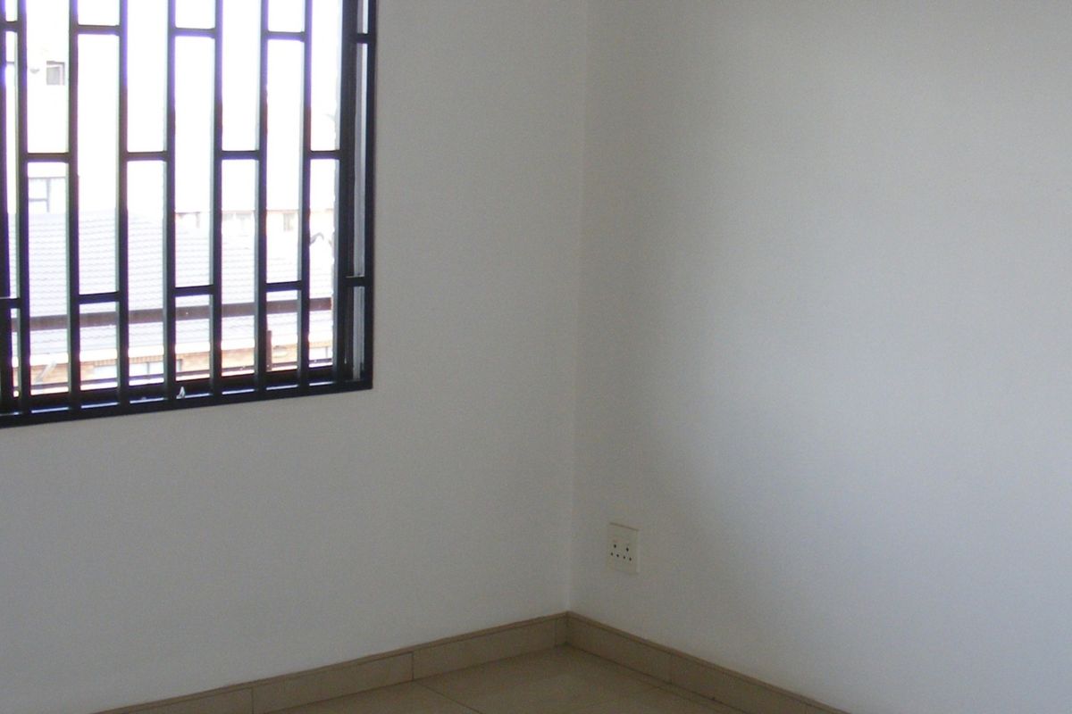 An empty bedroom featuring tiled flooring, white walls, and a window fitted with black security bars.