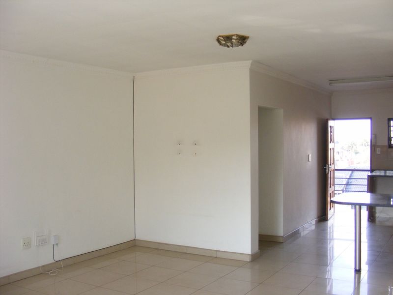 An open-plan living area featuring tiled flooring, neutral walls, and a seamless transition to the kitchen space, offering a bright and versatile layout.