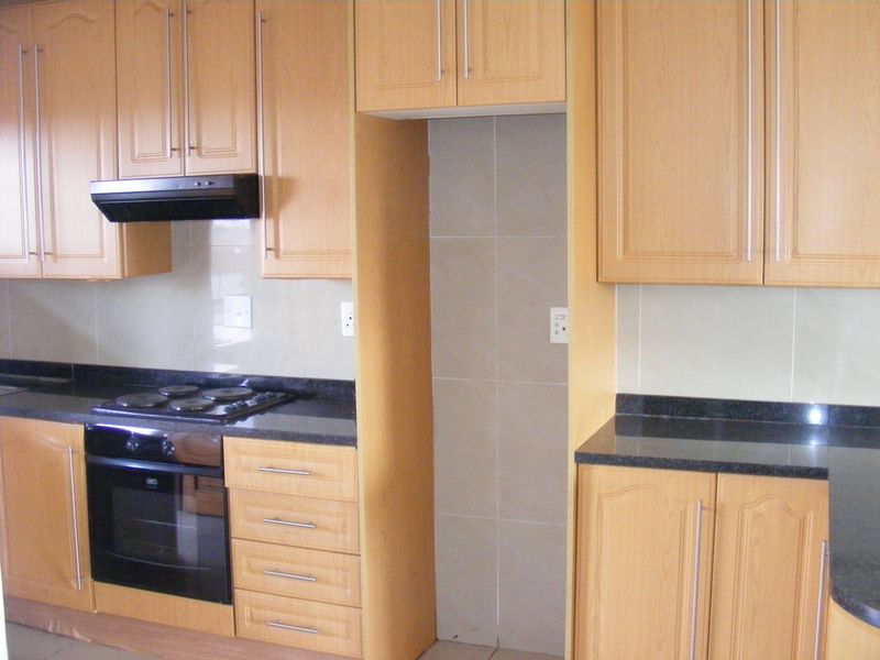 A functional kitchen featuring light wood cabinetry, dark granite countertops, a built-in oven, electric hob, and a dedicated space for a refrigerator.