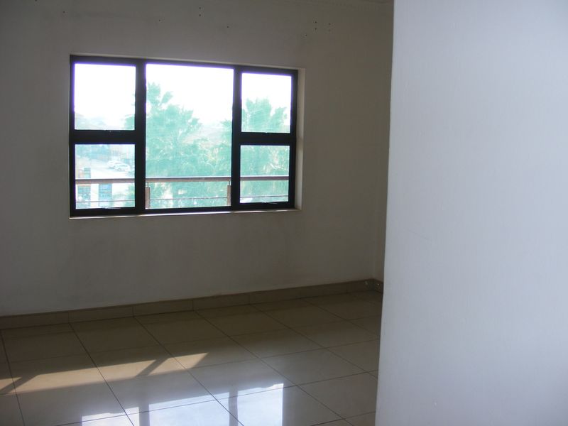 A bright, empty living area featuring neutral tiled flooring and large aluminium-framed windows that allow for ample natural light.
