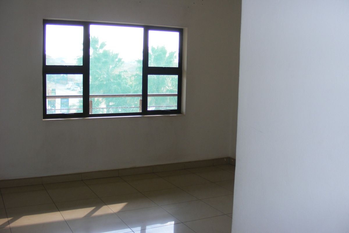 A bright, empty living area featuring neutral tiled flooring and large aluminium-framed windows that allow for ample natural light.