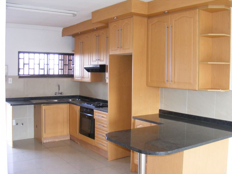 A functional kitchen featuring light wood cabinetry, dark granite countertops, a built-in oven, gas hob, and a convenient breakfast bar area.