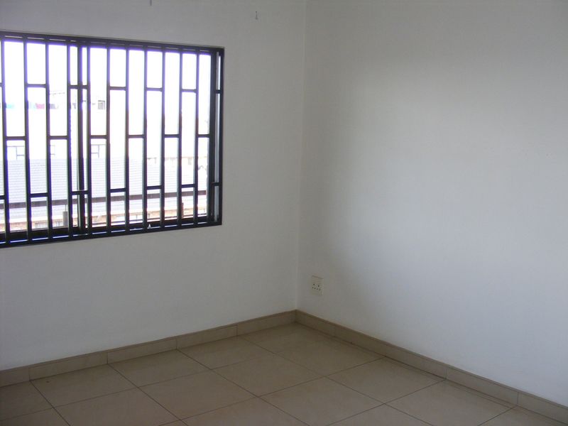 An empty bedroom featuring tiled flooring and a window fitted with security bars.