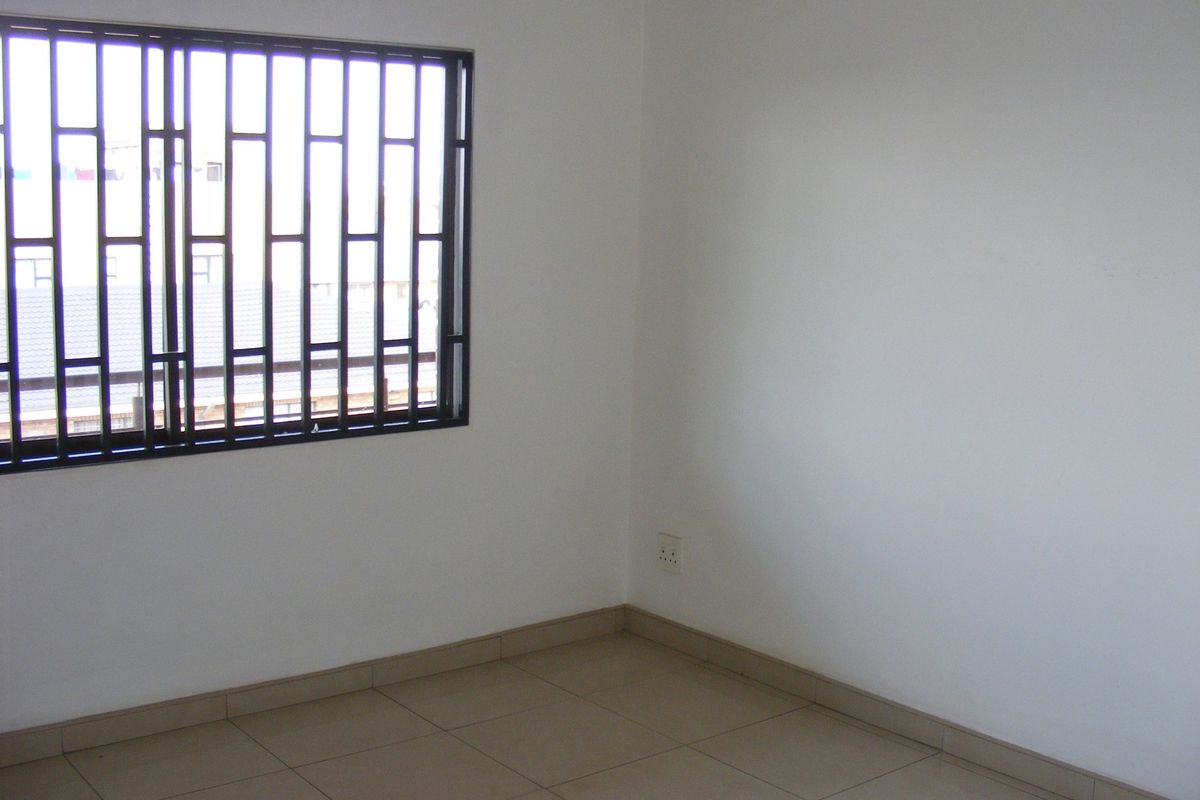An empty bedroom featuring tiled flooring and a window fitted with security bars.