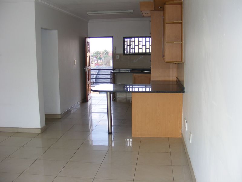 Open plan kitchen and living area featuring tiled flooring, built-in cabinetry with granite countertops, and a breakfast bar, leading to an exterior doorway.