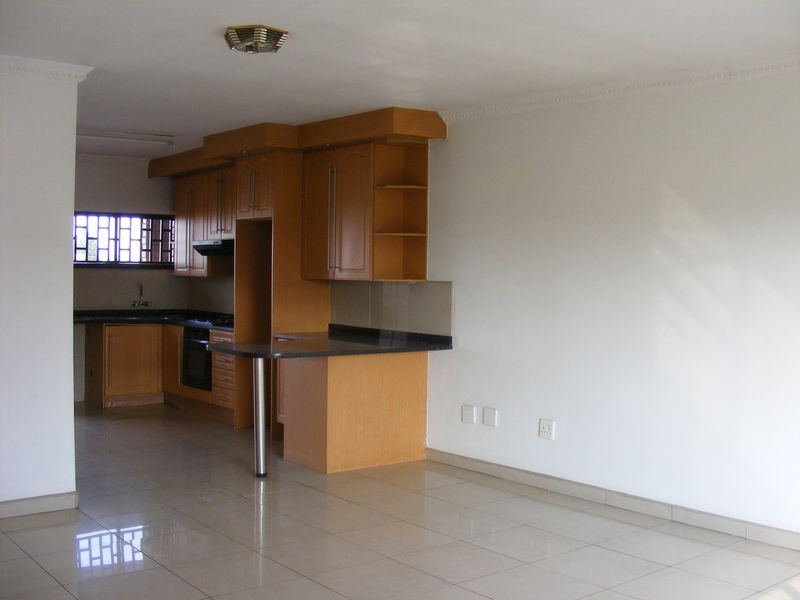 Open plan kitchen featuring wooden cabinetry, granite countertops, built-in oven, and tiled flooring, seamlessly integrated into the living area.