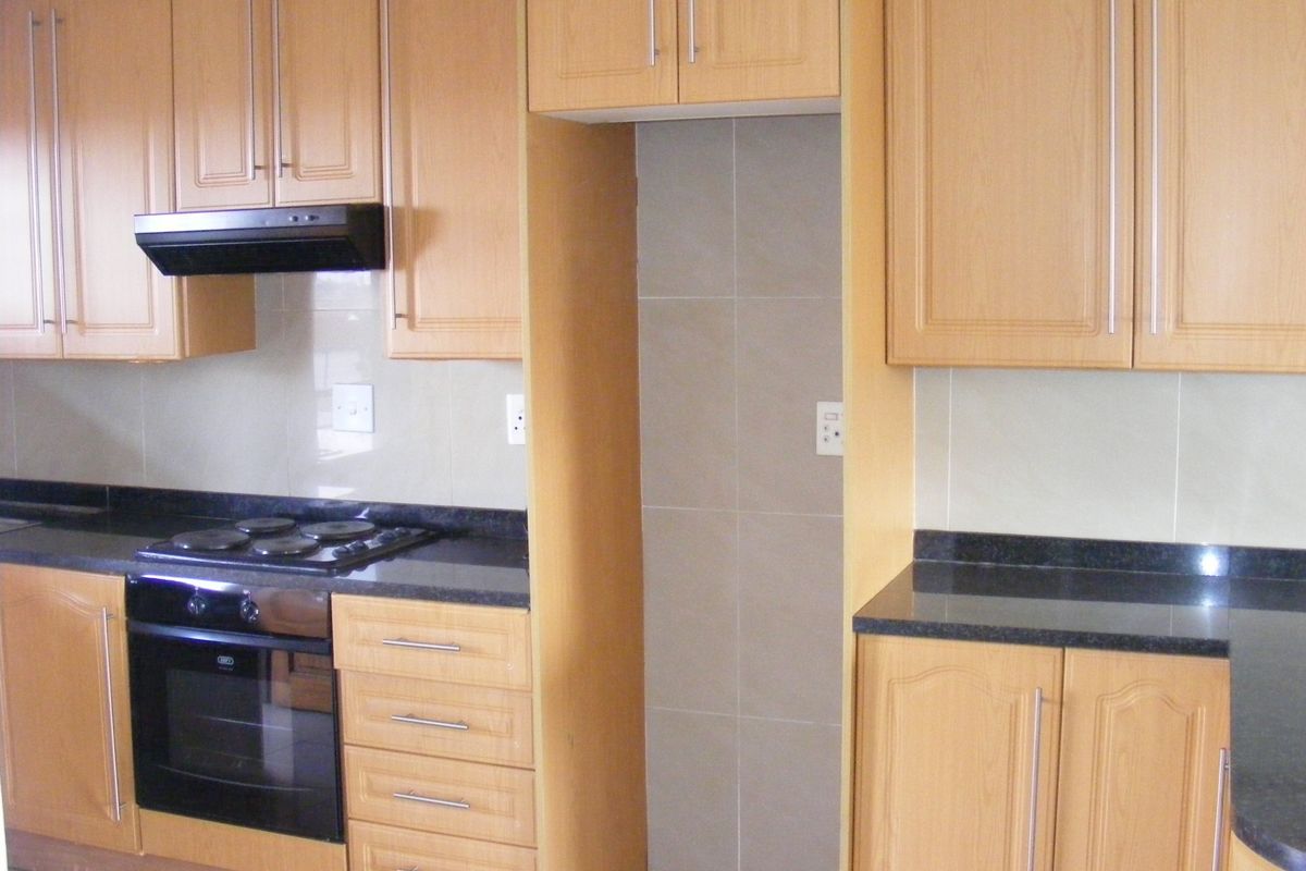 A functional kitchen featuring light wood cabinetry, dark granite countertops, a built-in oven, electric hob, and a dedicated space for a refrigerator.