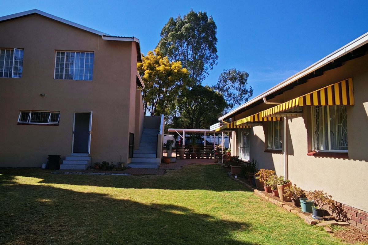 Rear view of the property featuring a spacious lawn, external staircase, and a covered patio area with striped awnings.