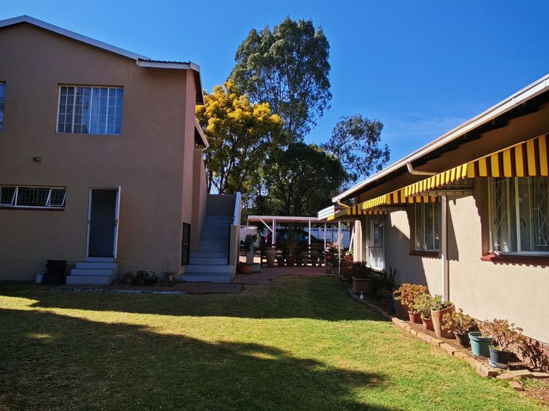 Rear view of the property featuring a spacious lawn, external staircase, and a covered patio area with striped awnings.