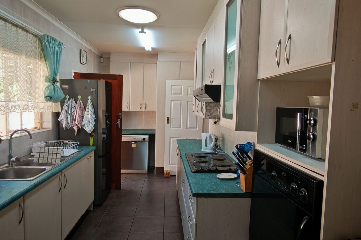 A functional galley-style kitchen featuring laminate cabinetry, contrasting countertops, built-in oven and hob, and tiled flooring with ample storage space.