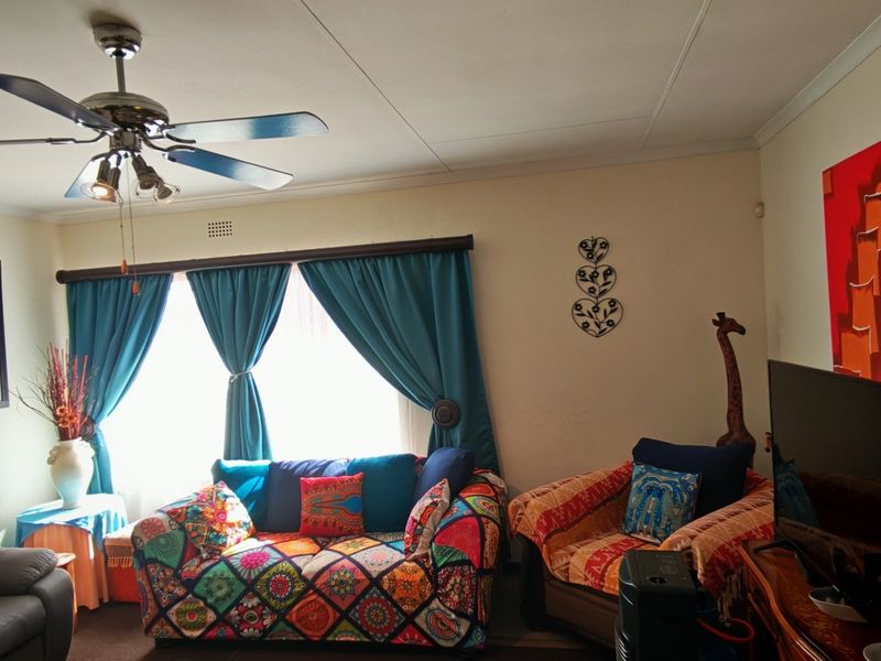 A comfortable living room featuring a ceiling fan and large window with curtain treatments, providing a functional and well-lit space.
