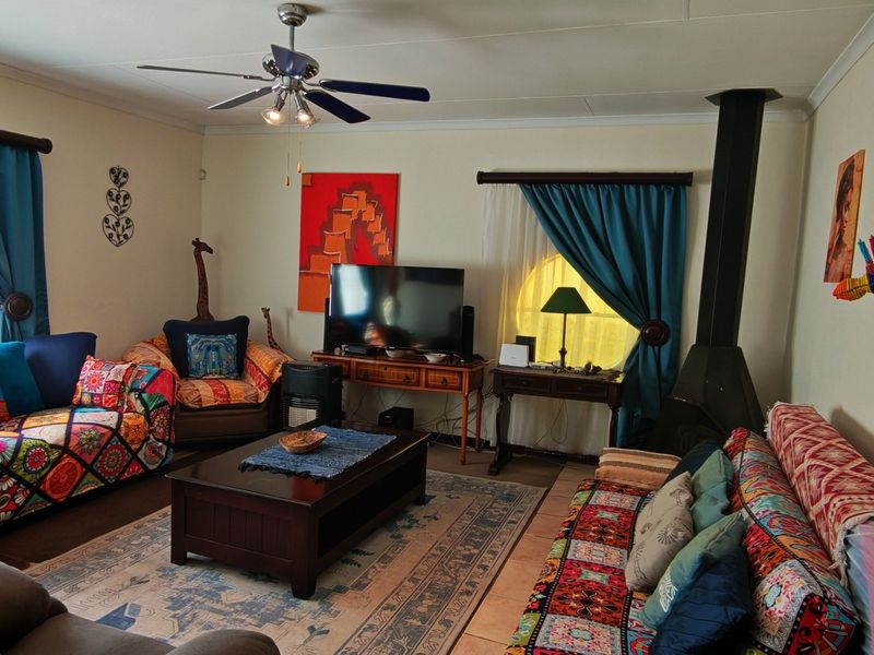 A comfortable living room featuring a freestanding fireplace, ceiling fan, and tiled flooring, offering a cozy space for relaxation.