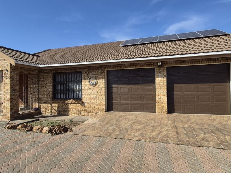 Front elevation of a face brick house featuring a double garage, tiled roof with solar panels, and a paved driveway.