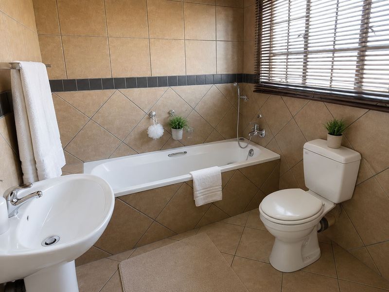 A functional bathroom featuring a pedestal basin, built-in bathtub with handheld shower, and toilet, finished with neutral-toned wall and floor tiles.