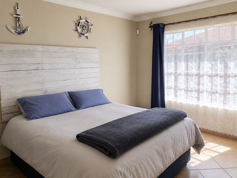 A well-maintained bedroom featuring neutral wall tones, tiled flooring, and natural light through a large window.