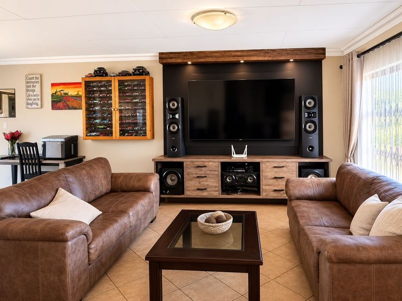A well-maintained living room featuring a custom built-in media unit, tiled flooring, and large windows with security gates.