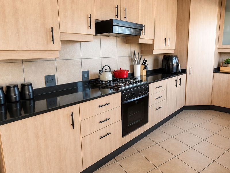 Modern kitchen featuring light wood cabinetry, black granite countertops, a gas hob, built-in oven, and neutral tiled flooring.