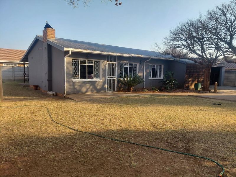 Rear view of a single-story house featuring a corrugated metal roof, brick chimney, and security-barred windows, set within a spacious garden area.
