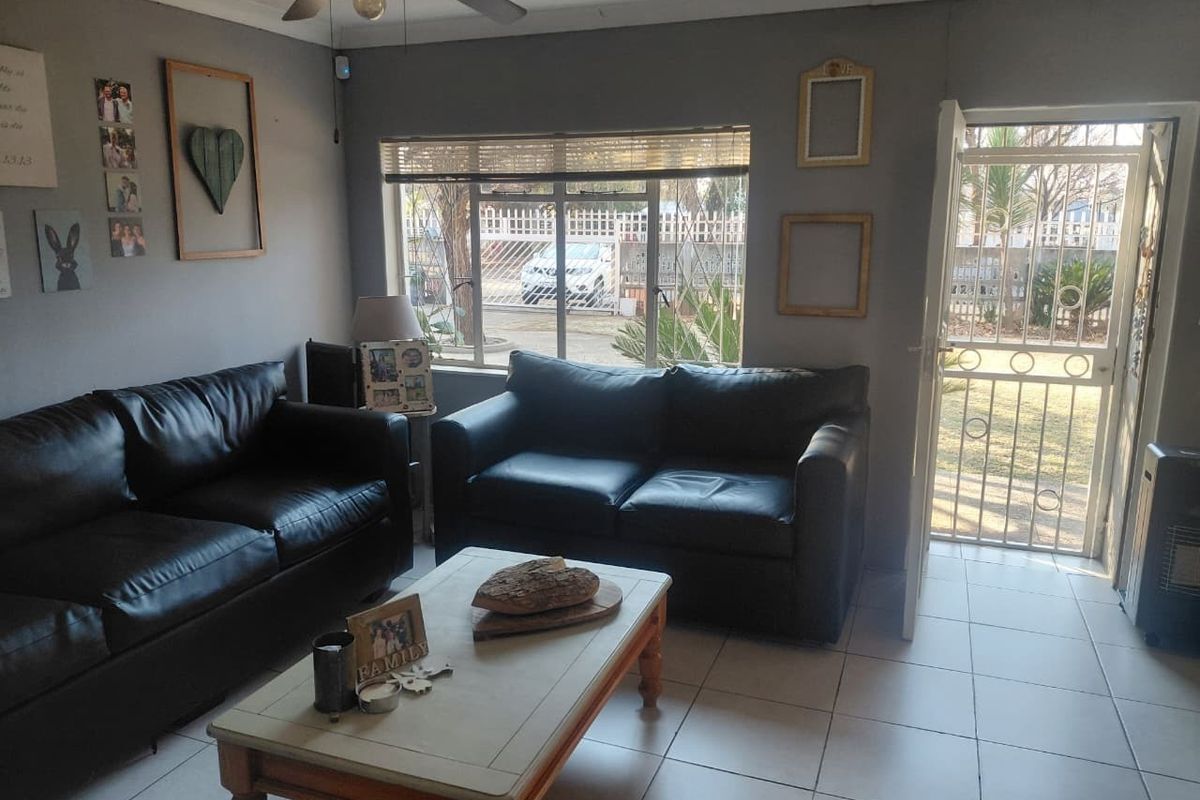 A comfortable living room featuring tiled flooring, a ceiling fan, and direct access to the front garden through a secure entrance door.
