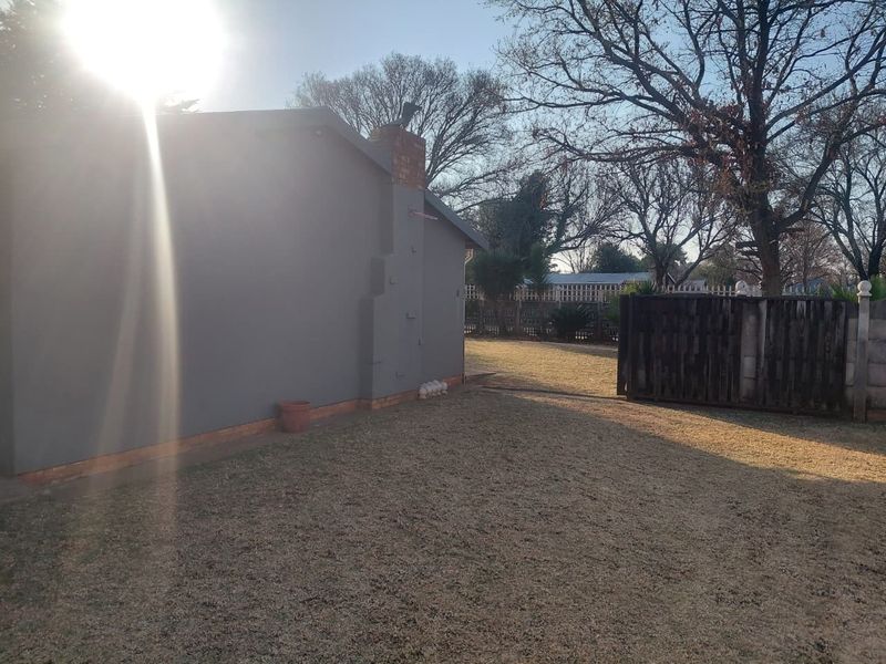 A view of the rear exterior of the house featuring a painted wall, brick chimney, and a spacious backyard lawn with perimeter fencing.