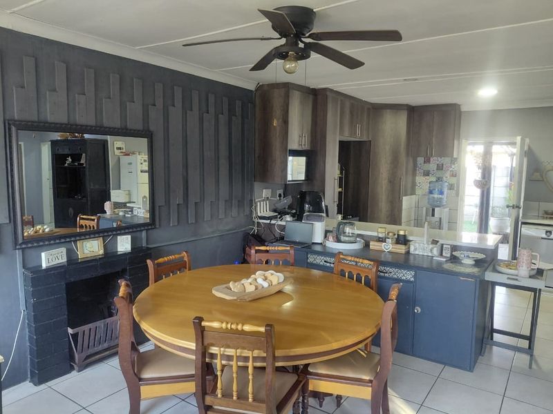 Open plan kitchen and dining area featuring dark cabinetry, a central kitchen island, tiled flooring, and a decorative feature wall with a ceiling fan.