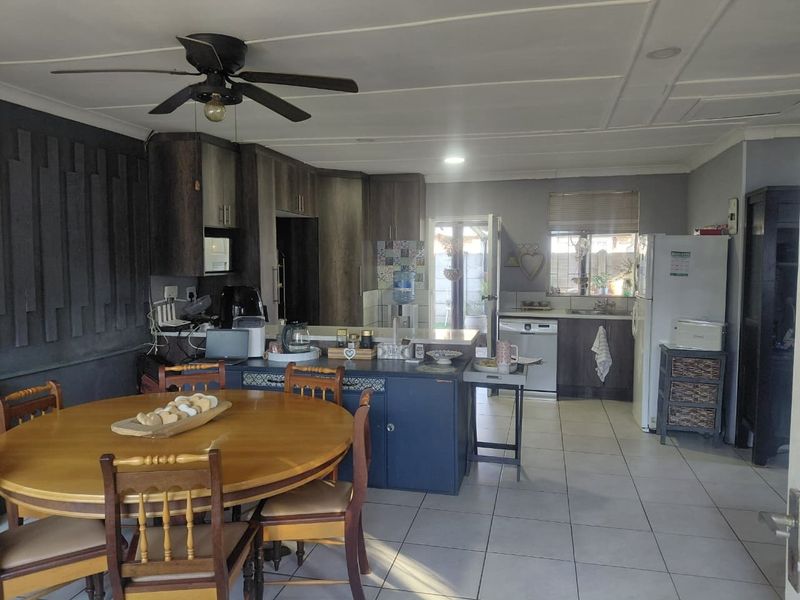 Open plan kitchen and dining area featuring tiled flooring, dark cabinetry, a central island, and a ceiling fan.