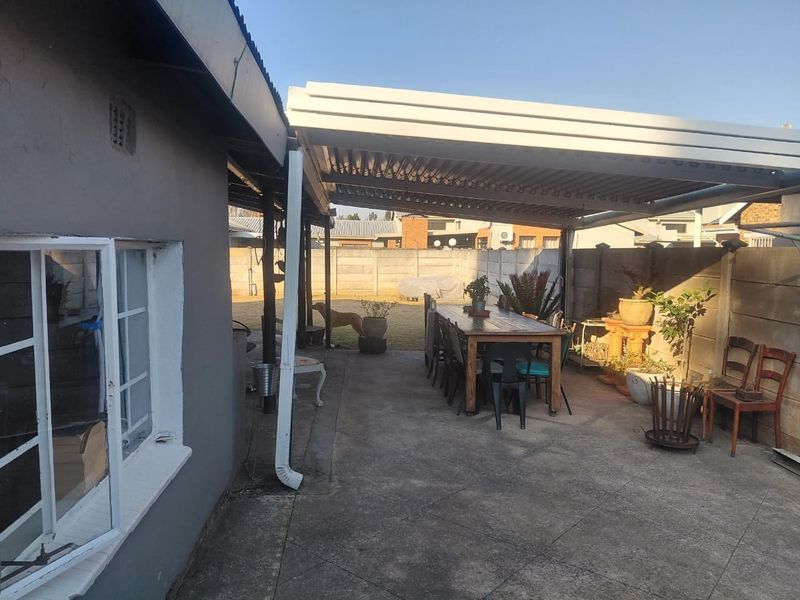 Covered outdoor patio area featuring a louvre roof system and concrete flooring, enclosed by a precast concrete boundary wall.