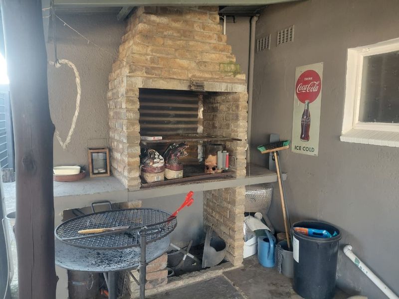 A covered outdoor patio area featuring a traditional built-in brick braai and concrete preparation surface, ideal for outdoor entertaining.