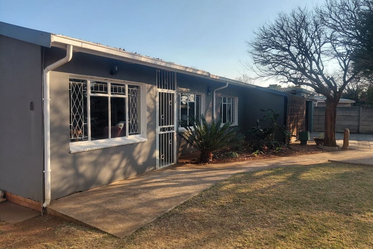 Rear view of the house featuring a paved walkway, security gates on windows and doors, and a low-maintenance garden area.
