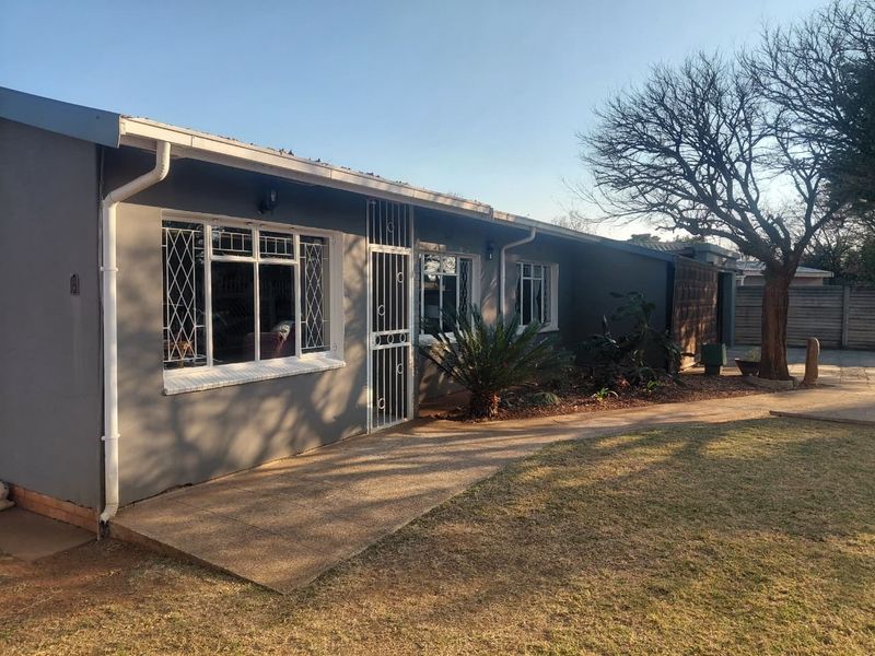 Rear view of the house featuring a paved walkway, security gates on windows and doors, and a low-maintenance garden area.