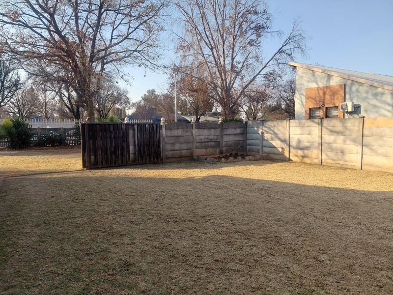 A spacious rear garden featuring a large lawn area, enclosed by a precast concrete boundary wall and a wooden gate.