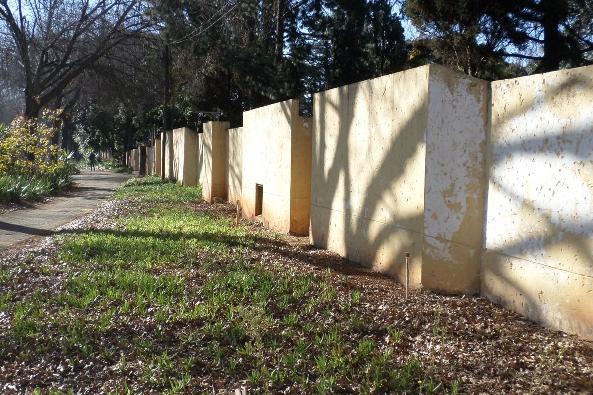 A view of the property boundary wall featuring a paved walkway and mature trees along the street frontage.