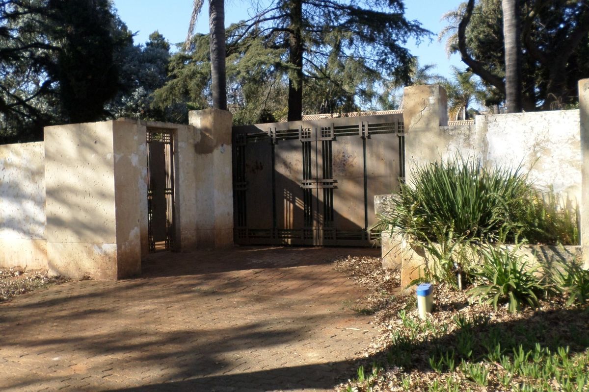 Front entrance featuring a paved driveway, metal security gates, and a perimeter boundary wall requiring maintenance.