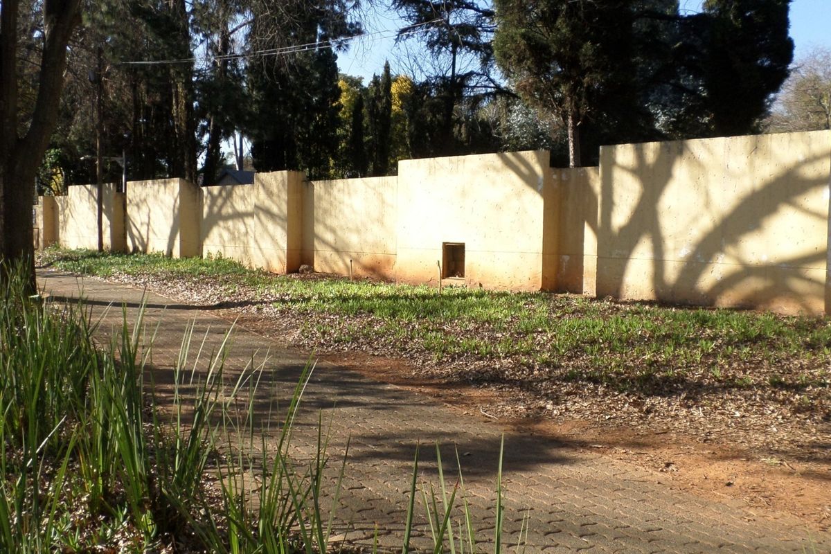 A view of the property's perimeter wall and adjacent paved walkway, showing signs of weathering and paint deterioration.