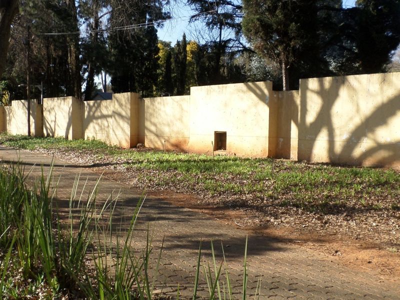 A view of the property's perimeter wall and adjacent paved walkway, showing signs of weathering and paint deterioration.