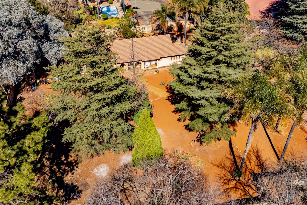 Aerial view of a residential property featuring a tiled roof house set within a large, tree-filled garden plot.