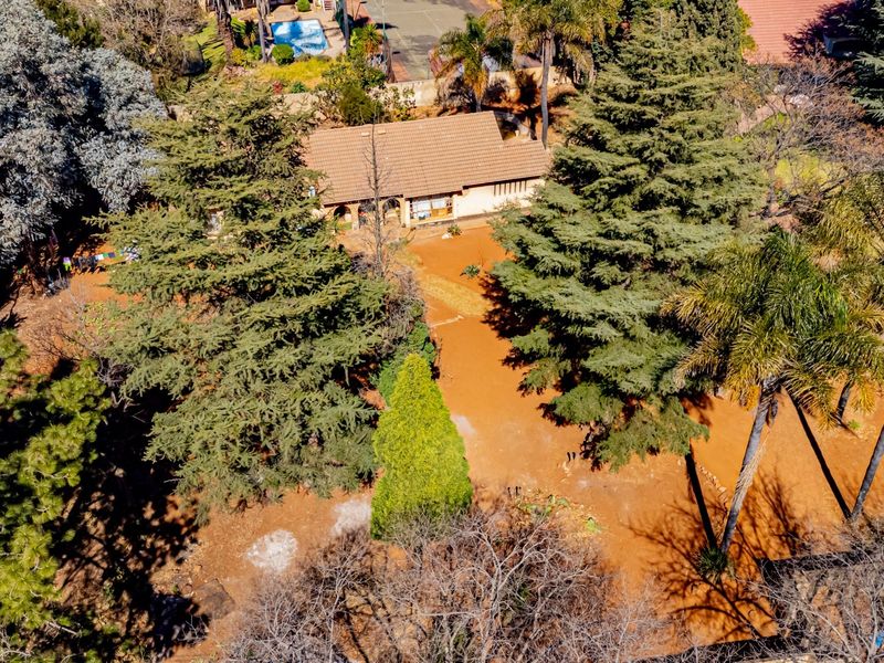 Aerial view of a residential property featuring a tiled roof house set within a large, tree-filled garden plot.