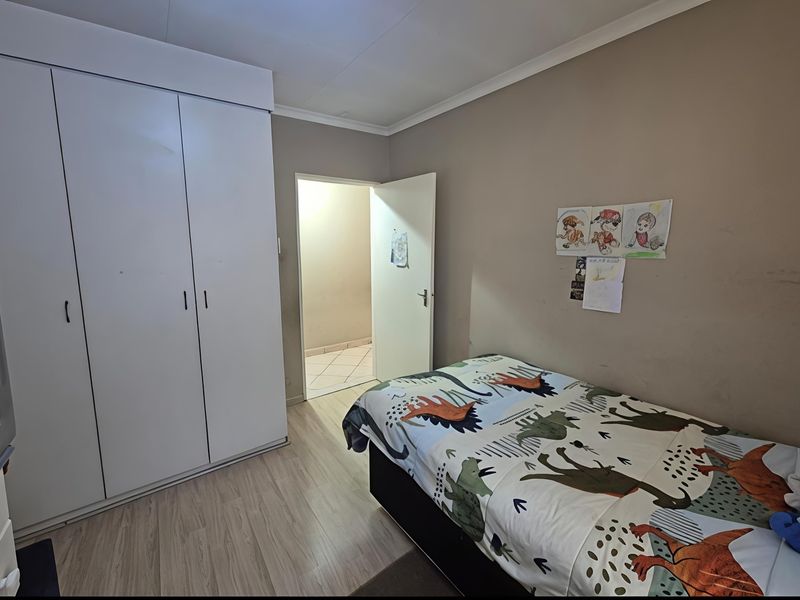 A functional bedroom featuring built-in cupboards, laminate flooring, and neutral wall tones, providing a practical space with direct access to an adjacent room.